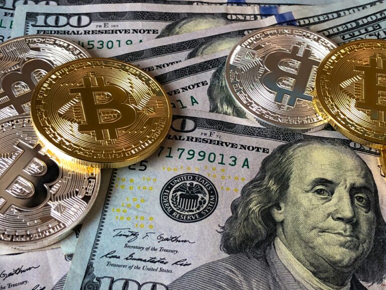 Close-up image of physical representations of Bitcoin placed on top of US hundred-dollar bills, symbolizing alternative income streams through digital currencies, relevant to the discussion on extra income apps.