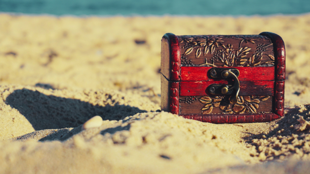 A small, intricately carved treasure chest rests partially buried in the sandy beach, symbolizing hidden treasures and insights, akin to the valuable data unearthed by Buffer Analytics in the competitive landscape of social media.