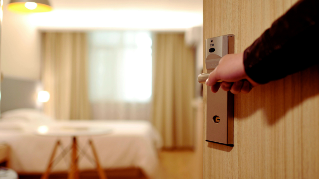 A person's hand is opening a modern electronic door lock to a well-lit, inviting hotel room, symbolizing the ease of starting with the Buffer tutorial for efficient social media management.