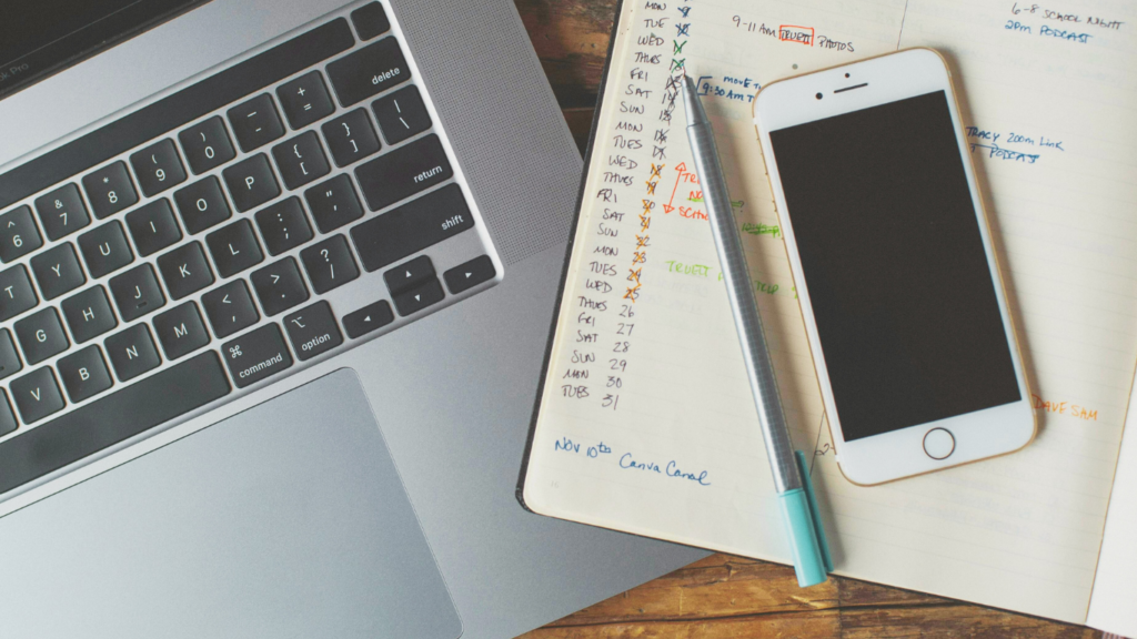 A workspace with a laptop, a smartphone, and a notepad filled with a handwritten posting schedule, illustrating the manual planning process that can be streamlined with Buffer's content scheduling feature.