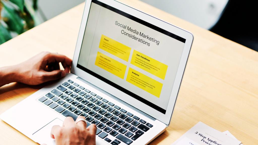 Hands of a person typing on a laptop that displays a presentation slide titled 'Social Media Marketing Considerations' with sections on reach, user-friendliness, and analytics.