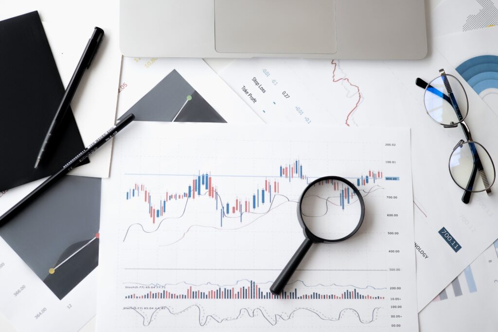 An analytical workspace with complex charts under the scrutiny of a magnifying glass, alongside a laptop, notepad, and a pair of glasses, symbolizing the detailed examination of social media metrics for strategic insights.