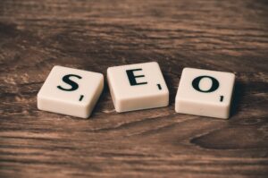 Three computer keyboard keys with the letters 'S', 'E', and 'O' laid out on a wooden surface, representing the acronym for Search Engine Optimization (SEO).