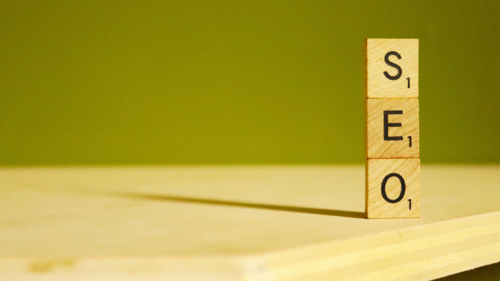 Wooden letter blocks spelling 'SEO' on a plain surface with a greenish-yellow backdrop, emphasizing the key concept of SEO basics.