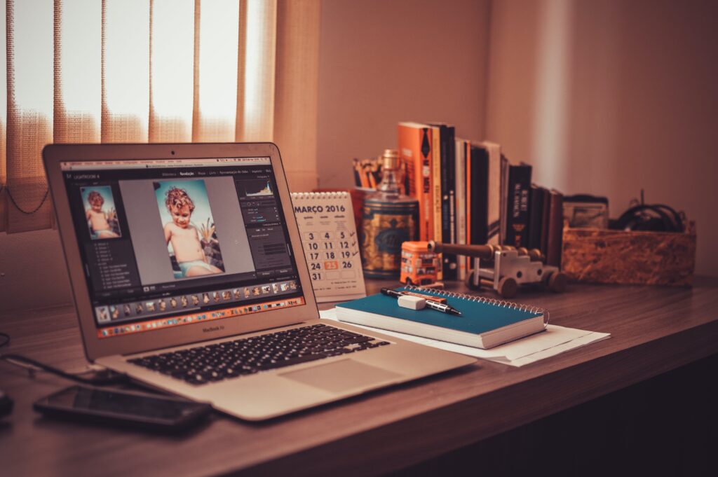 A home office environment showcasing a laptop with photo editing software, indicating a remote writing job workspace, complete with reference books and personal touches.