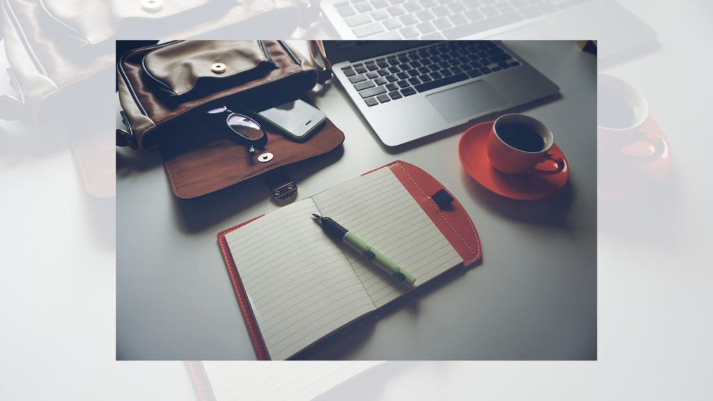 A well-organized workspace with a laptop, notebook, pen, smartphone, and a cup of coffee, ready for online content creation and communication.